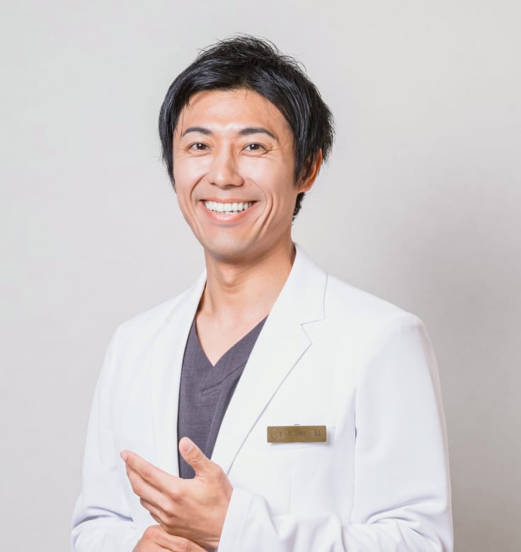 安心感と親しみやすさを感じさせる白衣を着た院長の小島 永稔の笑顔の写真